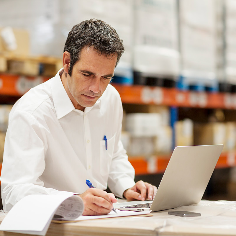 A man writing notes as he scrolls through his laptop.